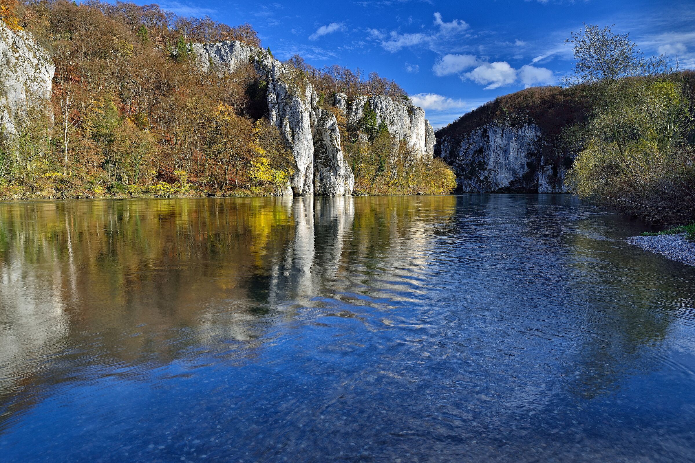 Donaudurchbruch im Herbst: blauer Fluss, herbstgelbes Laub, graue Felsen