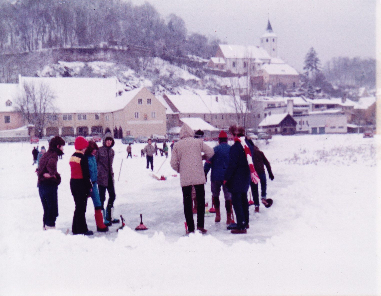 Eine Gruppe Menschen beim Eisstockschießen auf dem Donaustaufer Altwasser vor der Kulisse einer Wohnsiedlung.