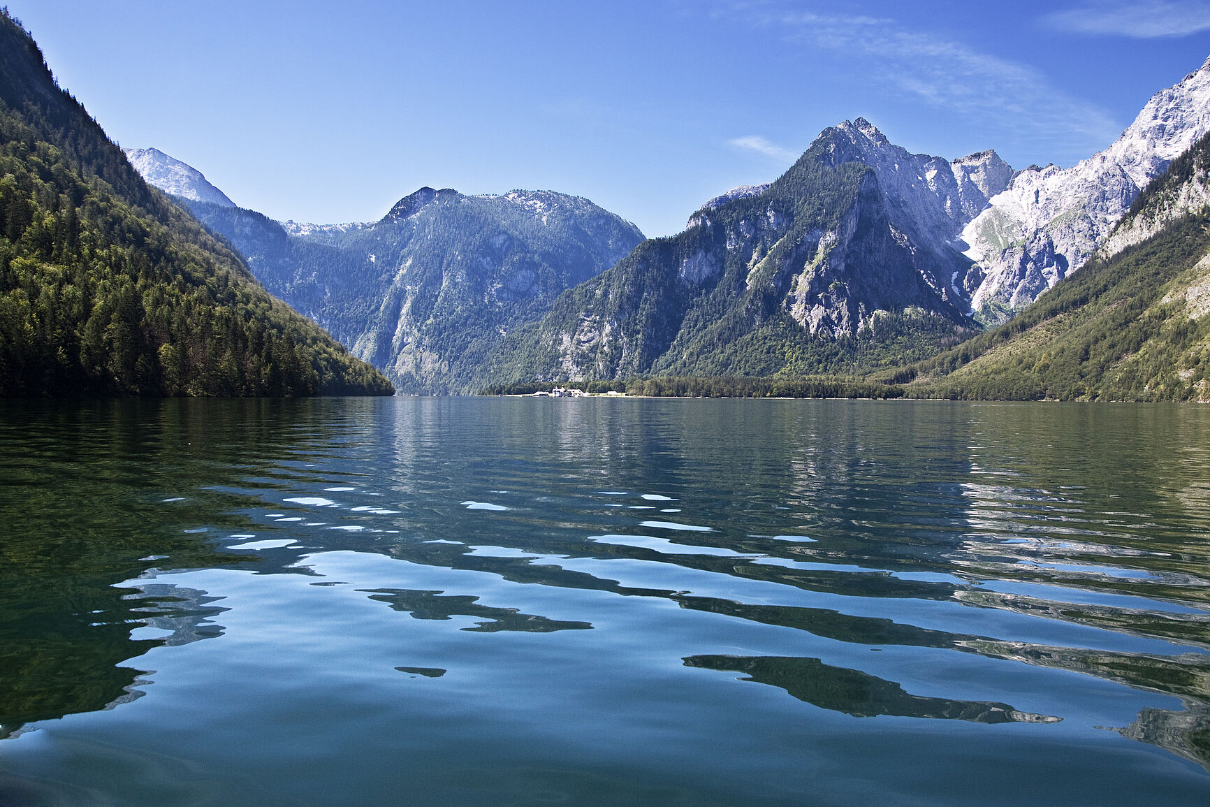 Das klare Wasser des Königssees im Vordergrund, im Hintergund die bis an die Baumgrenze bewaldeten Berge