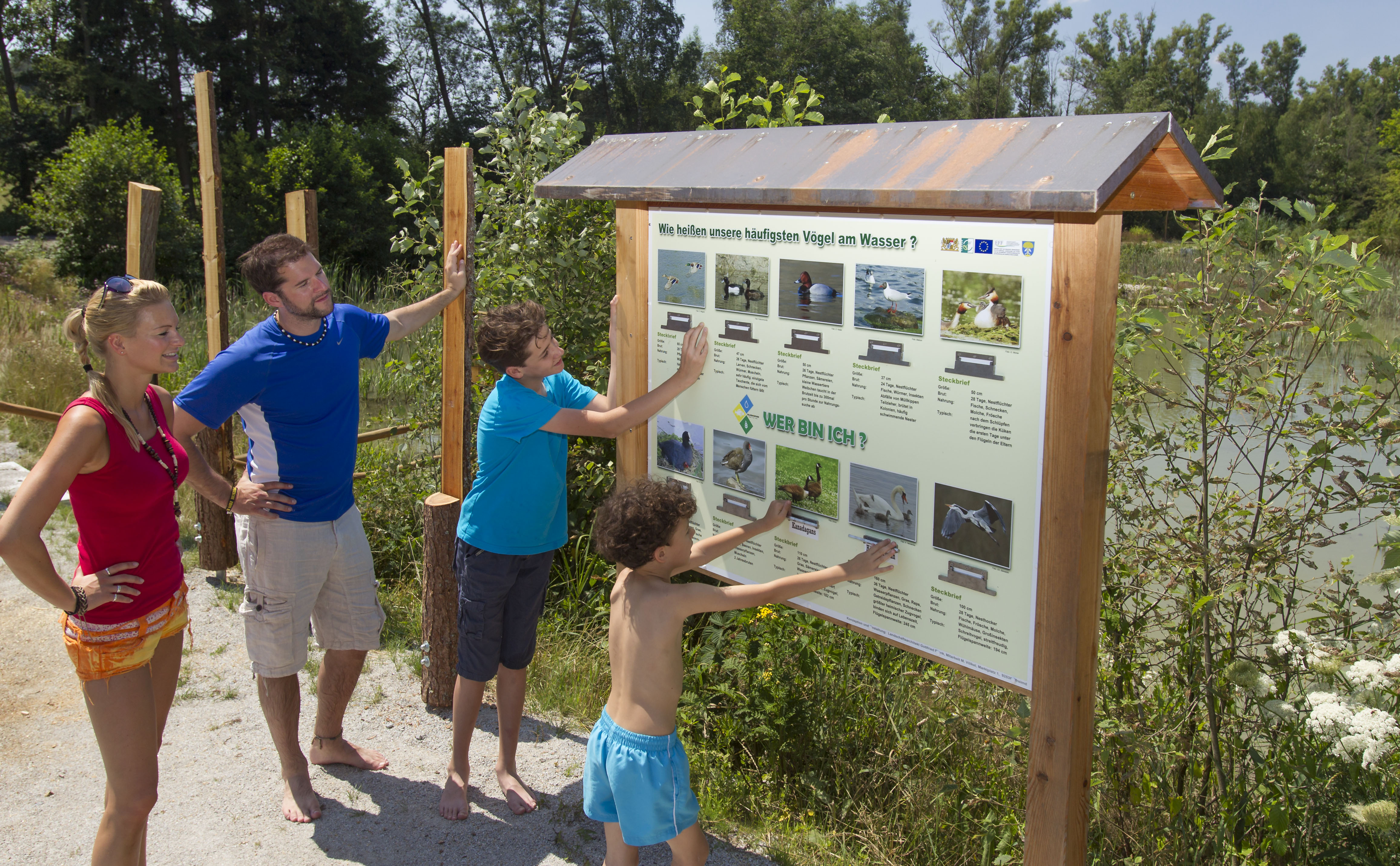 Tafel eines Naturlehrpfads, davor zwei Kinder und zwei Erwachsene: die Tafeln weisen heute den Weg (Foto: Zweckverband Oberpfälzer Seenland) 