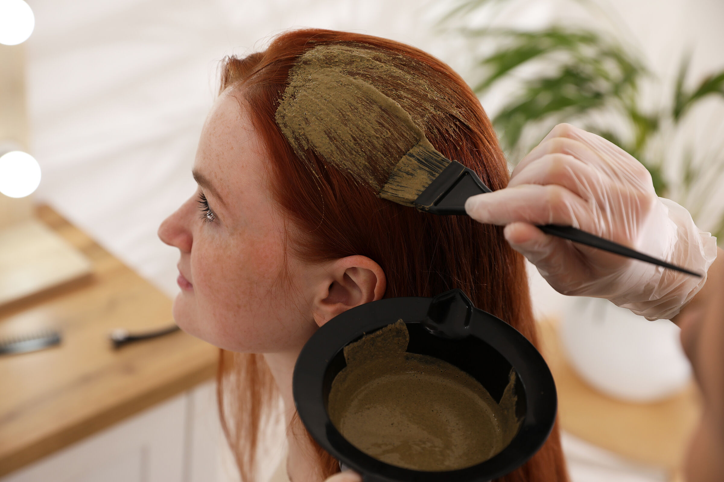 Die Haare einer Frau werden mit Hennafarbe bestrichen: Als Haarfarbe ist Henna in Deutschland zugelassen und darf den bedenklichen Stoff PPD enthalten. (Foto: New Africa/stock.adobe.com) 