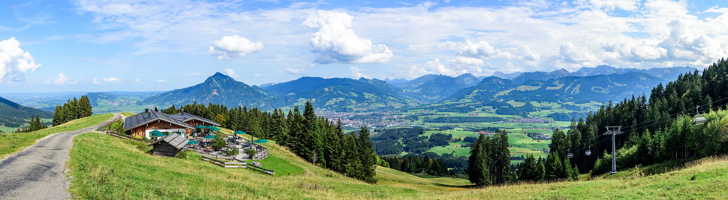 Ein asphaltierter Weg im sommerlichen Oberallgäu, im Hintergrund eine Skihütte sowie ein Lift