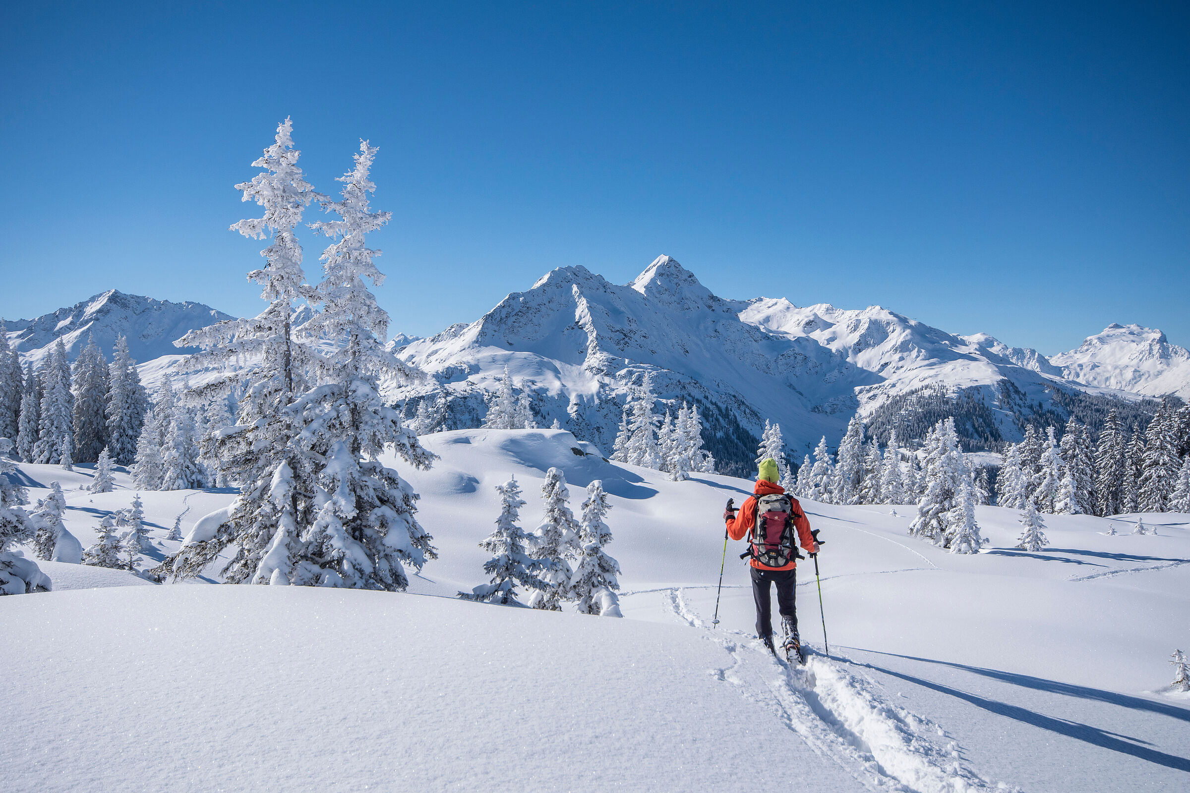 Winterwanderer in verschneiter Landschaft vor sonnenbeschienenem Gipfel