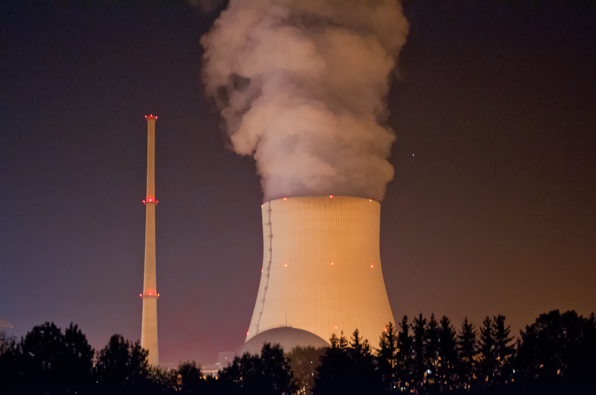 Das Atomkraftwerk Isar II bei Landshut in der Nacht: Vor dem dunklen Himmel steht der beleuchtete Kühlturm, aus dem Dampf in die Luft steigt.