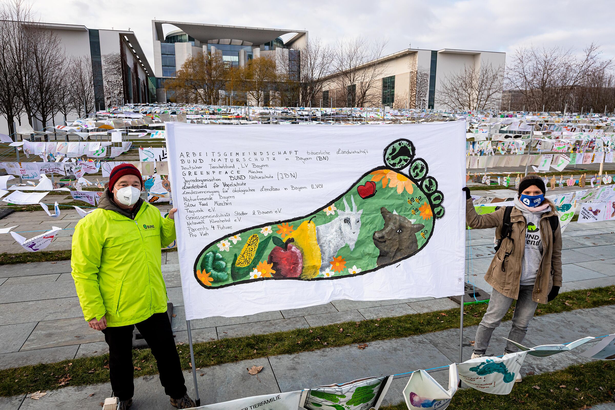 Agrarpolitik Bayern: Zwei Menschen in signalgelben Jacken und Mundschutz halten ein Demonstrationsbanner für einen besser Landwirtschaftspolitik hoch.