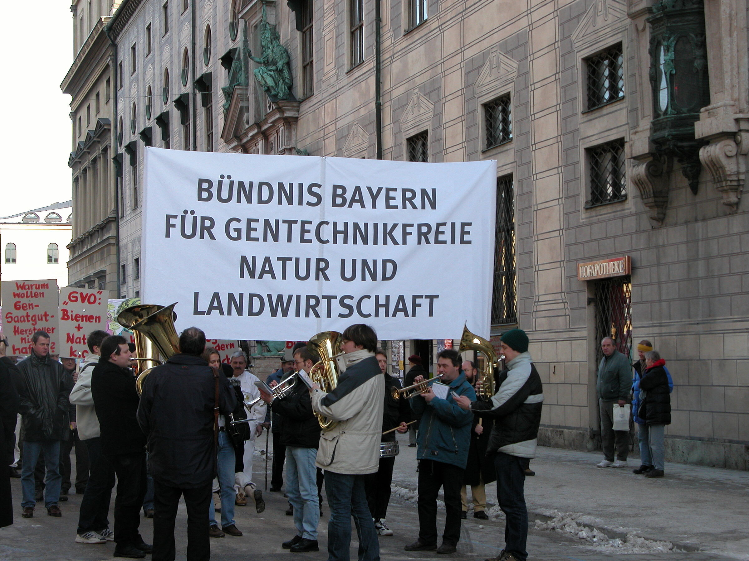 Mitglieder des Bündnis Bayern für gentechnikfreie Natur und Landwirtschaft demonstrieren mit einem großen weißen Banner und einer Blaskapelle in München