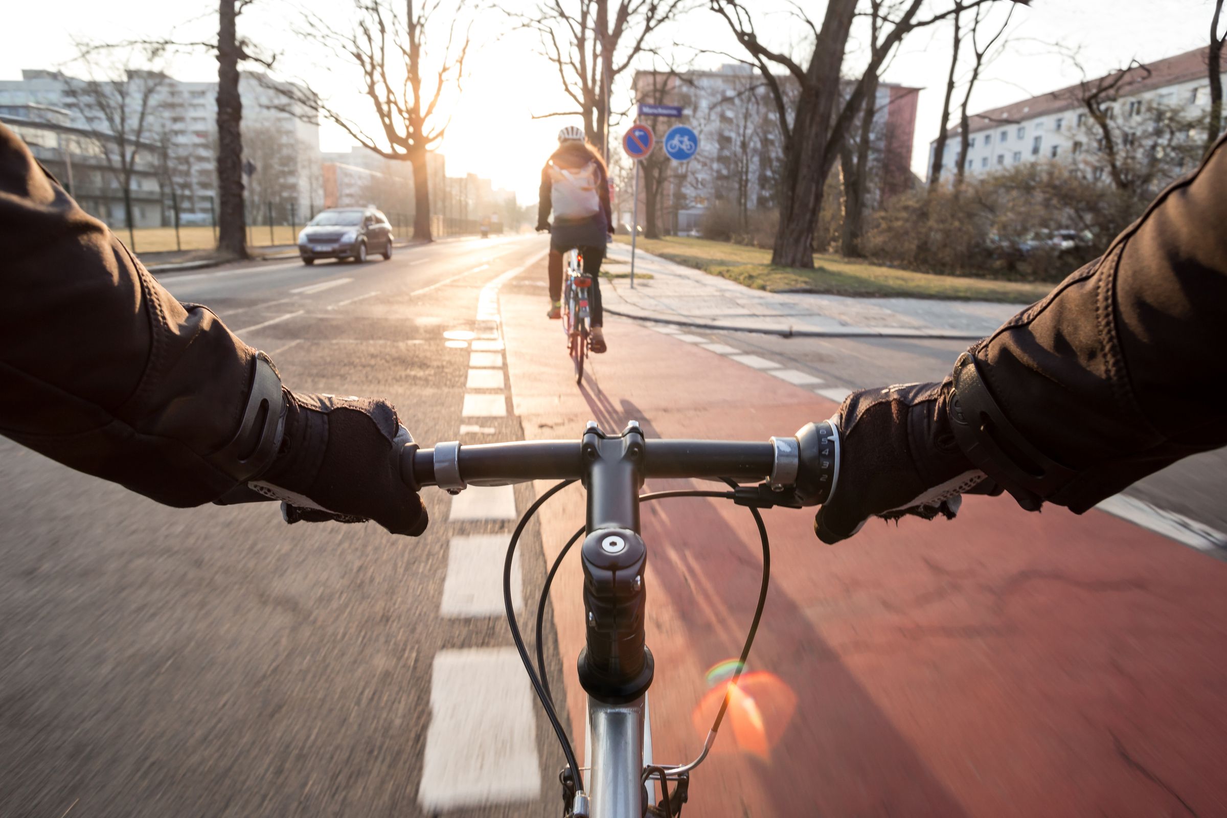 Zwei Radfahrer queren eine Kreuzung auf einem rot markierten Radweg: Sichere und schnelle Verbindungen sollen den Radverkehr zulasten des Autoverkehrs fördern (Bild: David.Sch - stock.adobe.com)