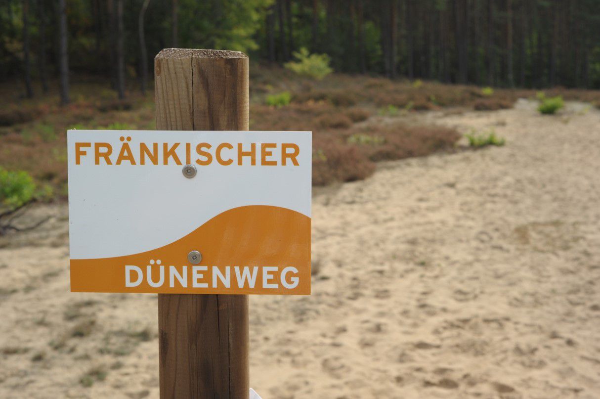 Ein Schild des Fränkischen Dünenwegs im Sand