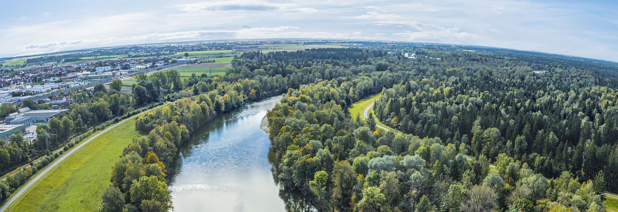 Der Lech heute südöstlich von Augsburg – mehr Kanal als Fluss. (ARochau/stock.adobe.com) Ein Fluss fließt in großem Bogen durch Wälder, am Rand sind Häuser zu sehen. (ARochau/stock.adobe.com)