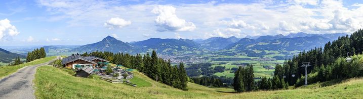 Werden Almwege ausgebaut, folgt darauf häufig eine intensivierte Nutzung – das gefährdet die Artenvielfalt der Almen. (Foto: ARochau/AdobeStock) Ein asphaltierter Weg im sommerlichen Oberallgäu, im Hintergrund eine Skihütte sowie ein Lift
