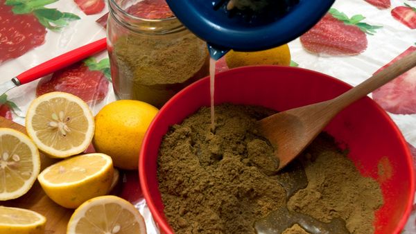 Henna richtig anwenden: In eine rote Schüssel mit grünlichem Hanna-Pulver wird Wasser geschüttet. Neben der Schüssel liegen Zitronen.