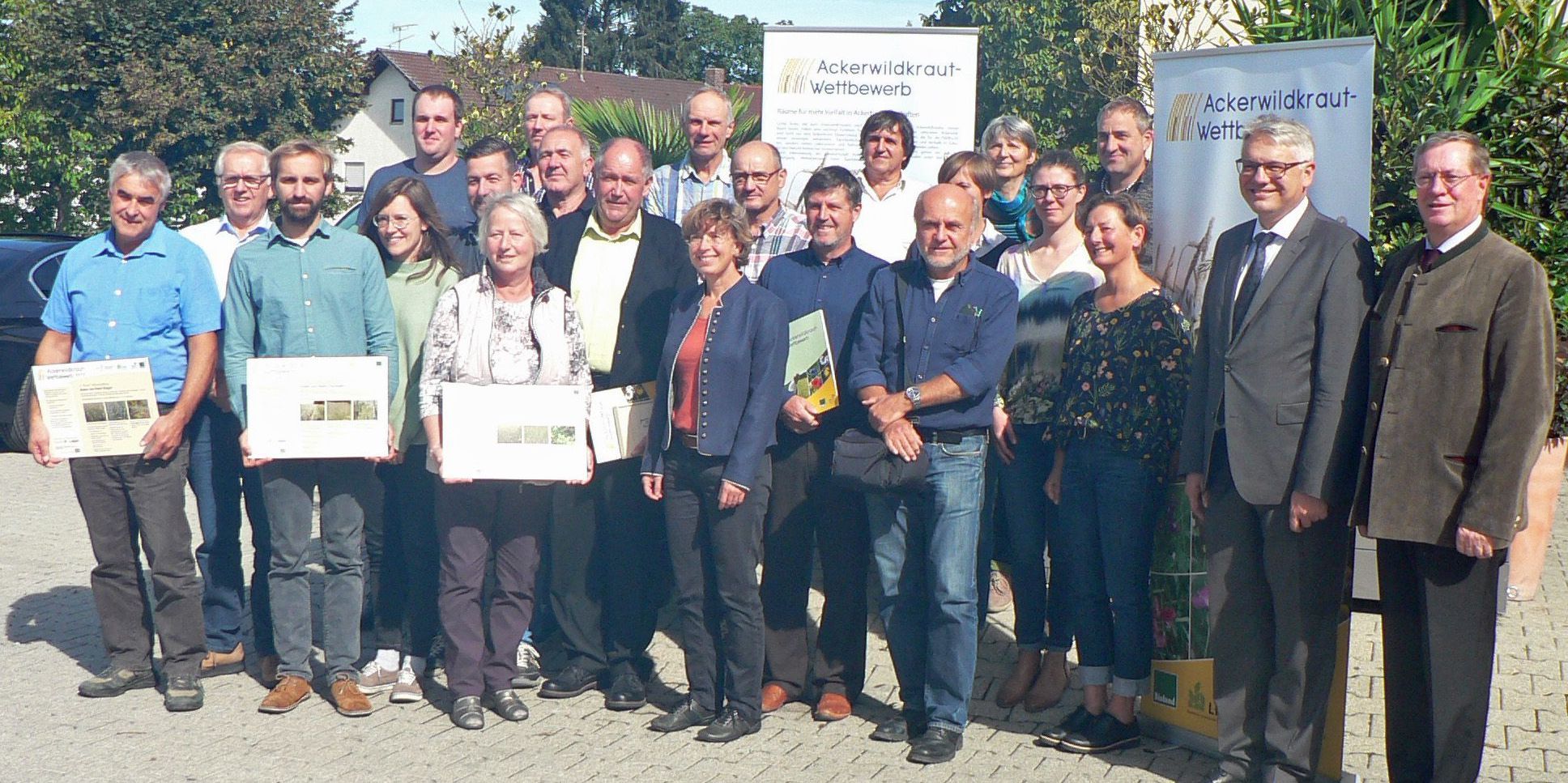 Eine Gruppe Leute steht vor zwei Werbebannern für den Ackerwildkraut-Wettbewerb. Einige haben Urkunden in der Hand. Mit dem Ackerwildkraut-Wettbewerb will der BN Landwirte ermutigen, mehr Vielfalt auf ihren Äckern zuzulassen. (Foto: LfL)