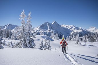 Winterwanderer in verschneiter Landschaft vor sonnenbeschienenem Gipfel
