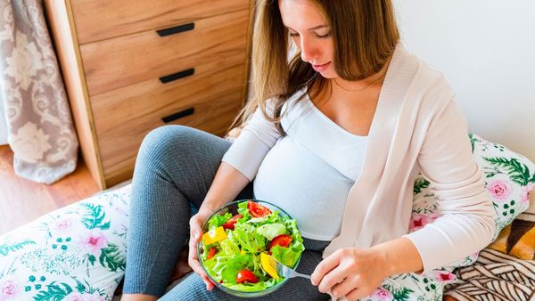Schwangerschaft ohne Schadstoffe: Eine schwangere Frau sitzt auf einem Sofa und ist Salat aus einer Schüssel.
