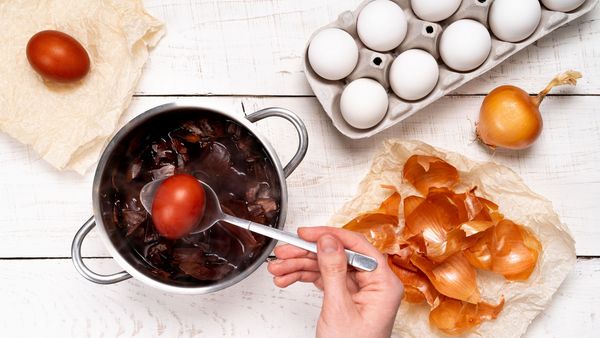 Ostereier natürlich färben: Eine weibliche Hand hebt ein in Zwiebelsud gefärbtes Ei mit einem Löffel aus einem Kochtopf. 