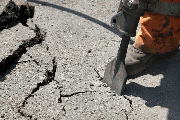 Eine Person, die mit einem Schlagbohrer Asphalt knackt und dadurch eine Fläche entsiegelt.