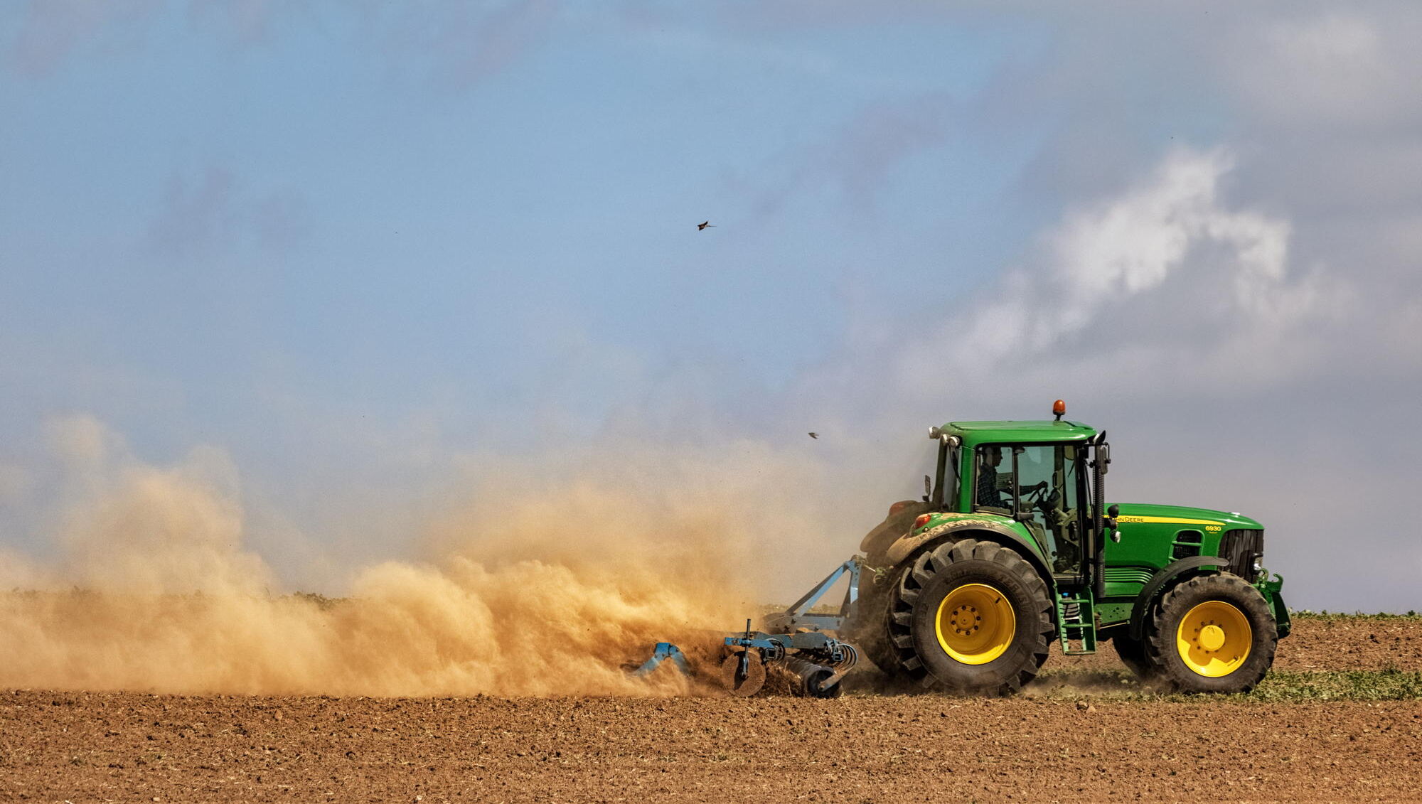 Landwirtschaft und Klimawandel: Traktor wirbelt Staub auf trockenem Acker auft t