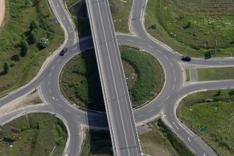 Welchen Weg nimmt der Straßenverkehr? (Bild: oroszgy - stock.adobe.com) Luftaufnahme eines Kreisverkehrs mit sechs Abzweigen: Der Straßenverkehr muss jetzt die richtige Ausfahrt nehmen, damit Flächenverbrauch und die zahlreichen negativen Auswirkungen verringert werden. (Bild: oroszgy/AdobeStock)