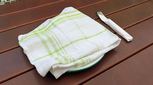EIn Geschirrtuch deckt das Essen auf einem Teller im Freien ab.