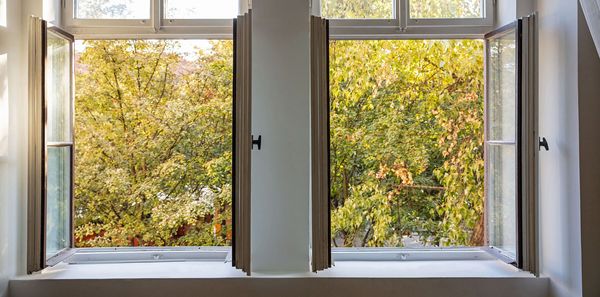 Klimaanlagen sind oft unnötig. Auch durch geschicktes Lüften kann man sommerwarme Räume sehr gut kühlen. (Foto: Rawf8/stock.adobe.com) Wohnung im Sommer kühlen ohne Klimaanlage: Durch zwei offene Fenster weht frische Luft in ein Zimmer.