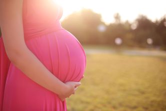 Für viele das größte Glück: Der Kinderwunsch geht in Erfüllung (Foto: Victoria Andreas/fotolia.com) Eine hochschwangere Frau steht in ein pinkes Gewand gekleidet bei Sonnenschein auf einer Wiese.