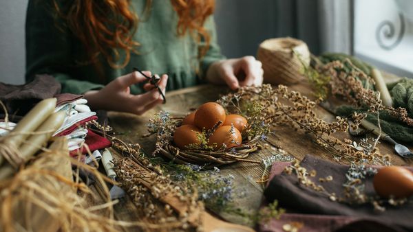 Ostern nachhaltig feiern: Eine Frau sitzt an einem Tisch und bastelt ein Osternest aus Naturmaterialien.