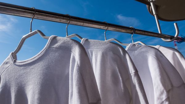Die Pflege Ihrer Kleidung ist der einfachste und effektivste Weg, ihre Lebensdauer zu verlängern. Oft hilft schon Lüften statt Waschen. (Foto: aomas/stock.adobe.com) Nachhaltige Kleidung: Vier weiße Pullover hängen im Freien zum Lüften. Im Hintergrund blauer Himmel.