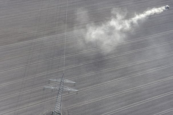 Kahler Ackerboden so weit das Auge reicht ohne Bäume oder Hecken, ein Traktor wirbelt Staub auf. Die heutige Agrarpolitik fördert solche großen Strukturen (Foto: Klaus Leidorf)