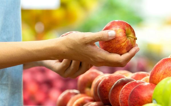 Nicht nur der Transportweg wirkt sich darauf aus, wie umweltfreundlich ein Lebensmittel ist. (Foto: paulovilela/stock.adobe.com) Eine Frau steht im Supermarkt und hält in jeder Hand einen Apfel
