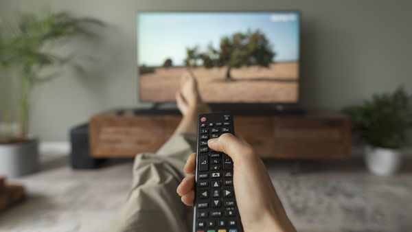 Fernsehgeräte gehören zu den größten Stromverbrauchern. Sowohl beim Kauf als auch im Betrieb lässt sich viel Energie und Geld sparen. (Foto: stokkete/stock.adobe.com) Strom sparen beim Fernsehen: Eine Frau sieht fern und hält die Fernbedienung in der Hand.