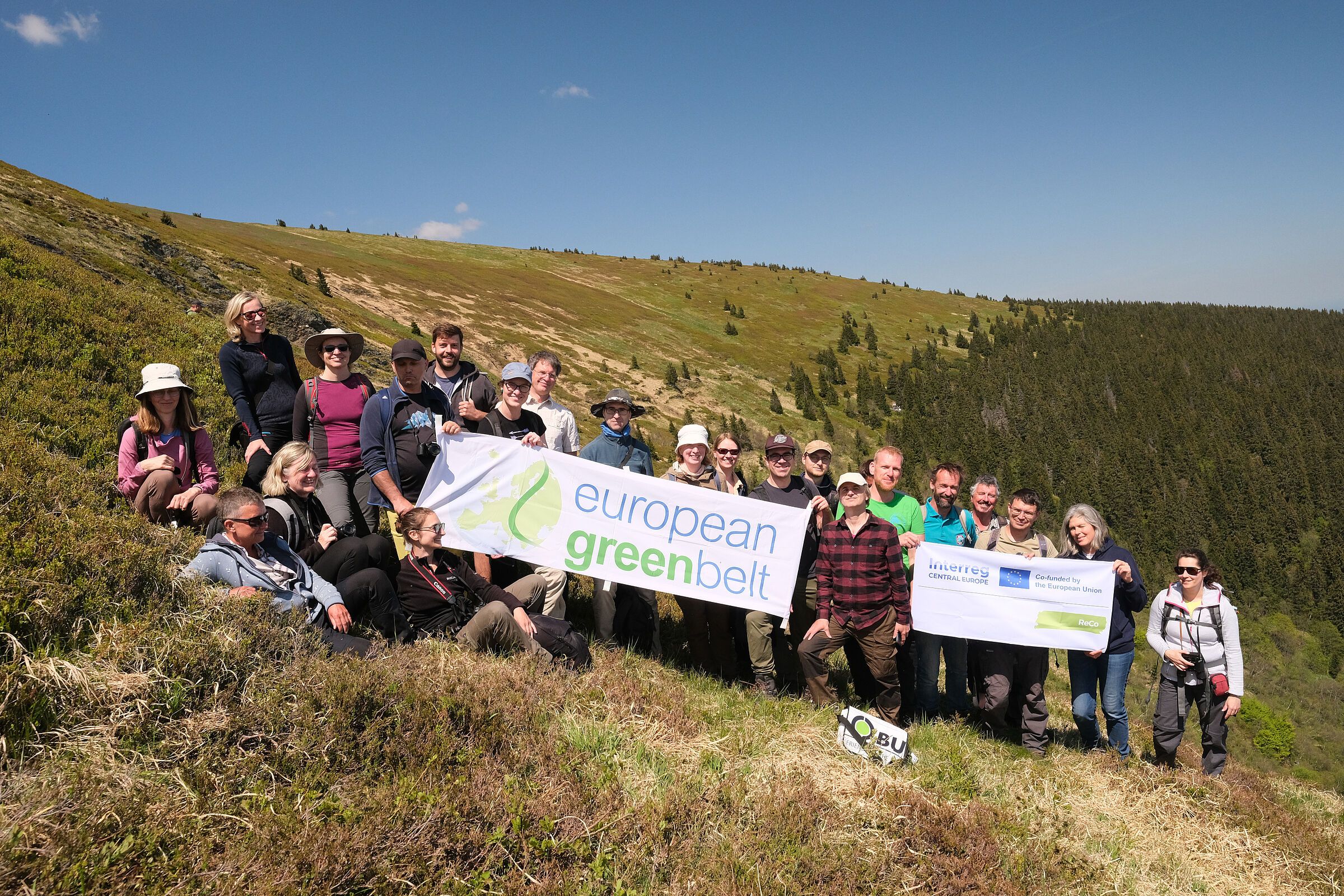 Exkursion der ReCon-Projektpartner: Eine große Gruppe von Menschen im bergigen Gelände mit einem Wald im Hintergrund, einige Menschen halten Transparente, eines mit der Aufschrift "european greenbelt" (Foto: BN)