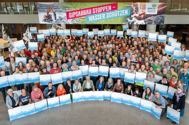 Die Delegierten des BUND Naturschutz stehen in einer großen Gruppe beieinander und halten Schilder mit symbolischen Wellen, um für mehr Wasserschutz zu demonstrieren.