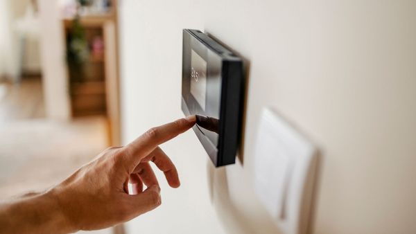 Richtig heizen: Ein Mann programmiert den an der Wand hängenden Thermostaten für die Heizung.