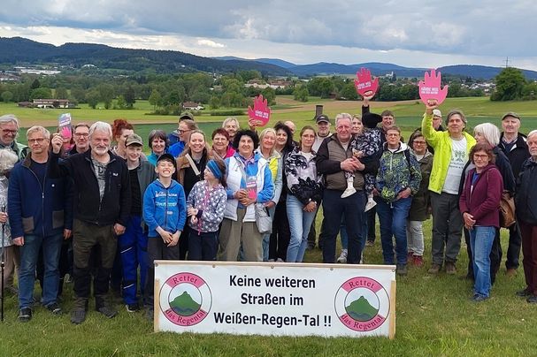 260517_Exkursion_Aktionsbündnis Regental_ Hr. Meindl Ca. 35 Leute stehen im Talraum vor einem Banner "Keine weiteren Straßen im Weißen-Regen-Tal", 3 davon halten eine rote Hand hoch mit der Aufschrift "Hands off Nature"