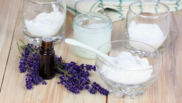 Deo selber machen: Auf einer Tischplatte stehen Glasschüsselchen mit Zutaten für ein selbst gemachtes Deo - darunter Natron und Speisestärke - sowie ein Fläschchen mit Lavendelöl.