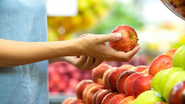 Discounter-Bio: Eine Frau hält einen Apfel in der Hand und begutachtet ihn.