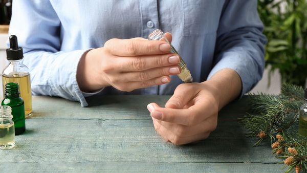 Deo selber machen: Eine Frau sitzt an einem Holztisch und fährt mit einem selbst befüllten Deoroller in einer kleinen Glasflasche über ihre Hand.